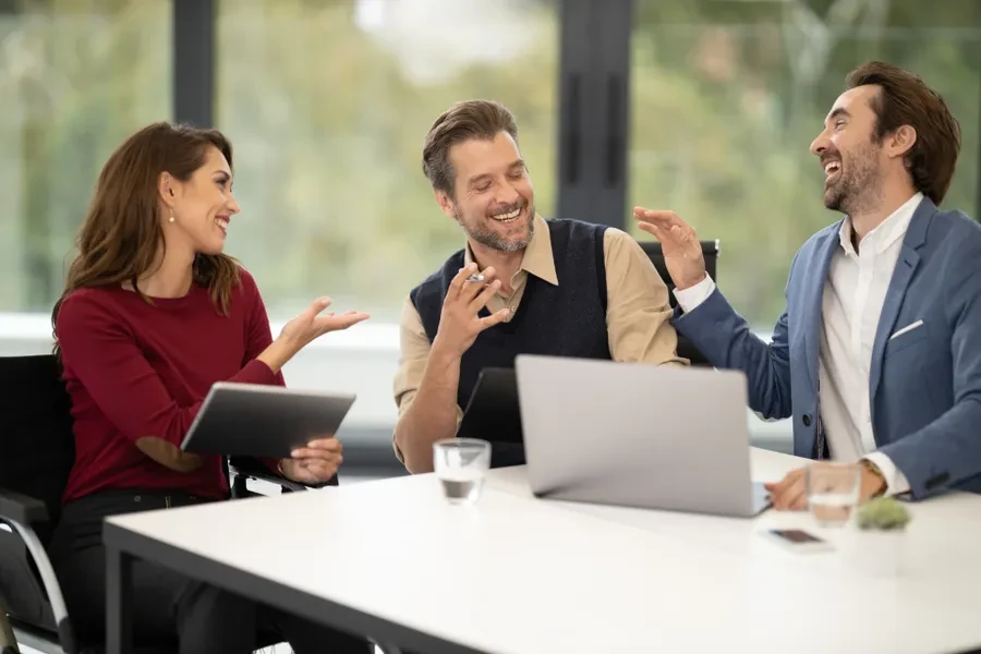 Tres profesionales conversando con portátiles sobre la mesa en una reunión de trabajo