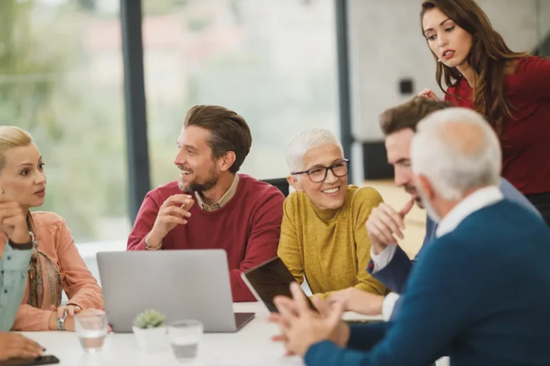 Un equipo de personas de distintas edades se ríe alrededor de una mesa de reuniones