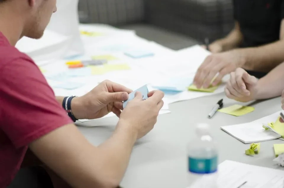 Varias personas trabajan alrededor de una mesa con notas adhesivas de colores y teléfonos móviles