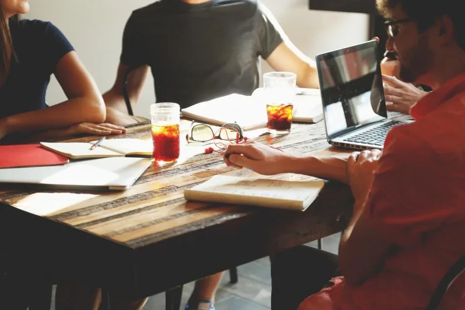 Un equipo conversa alrededor de una mesa de madera con cuadernos y un portátil