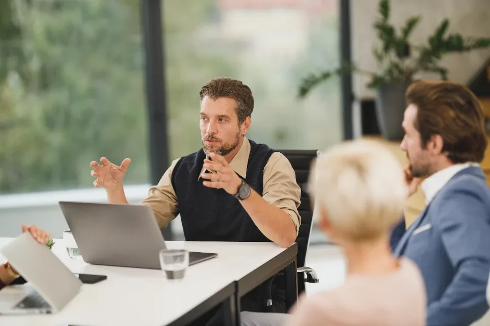 Un responsable conversa con su equipo alrededor de una mesa con portátiles