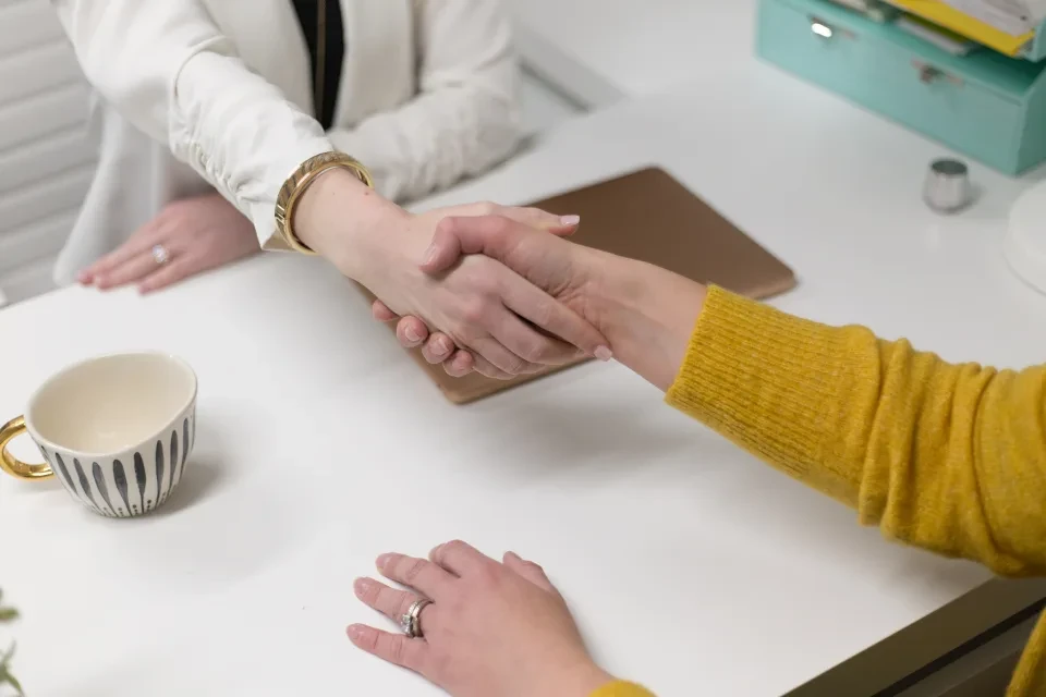 Dos personas se dan la mano sobre una mesa de trabajo al cerrar una contratación