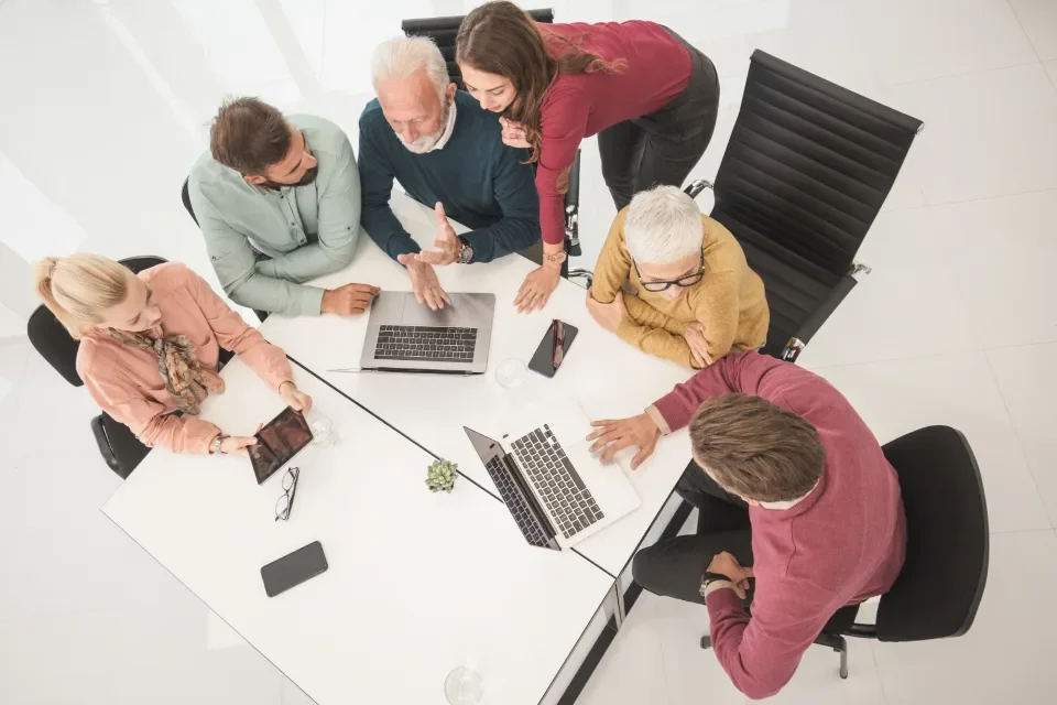 Vista cenital de un equipo de cinco personas trabajando con portátiles alrededor de una mesa blanca