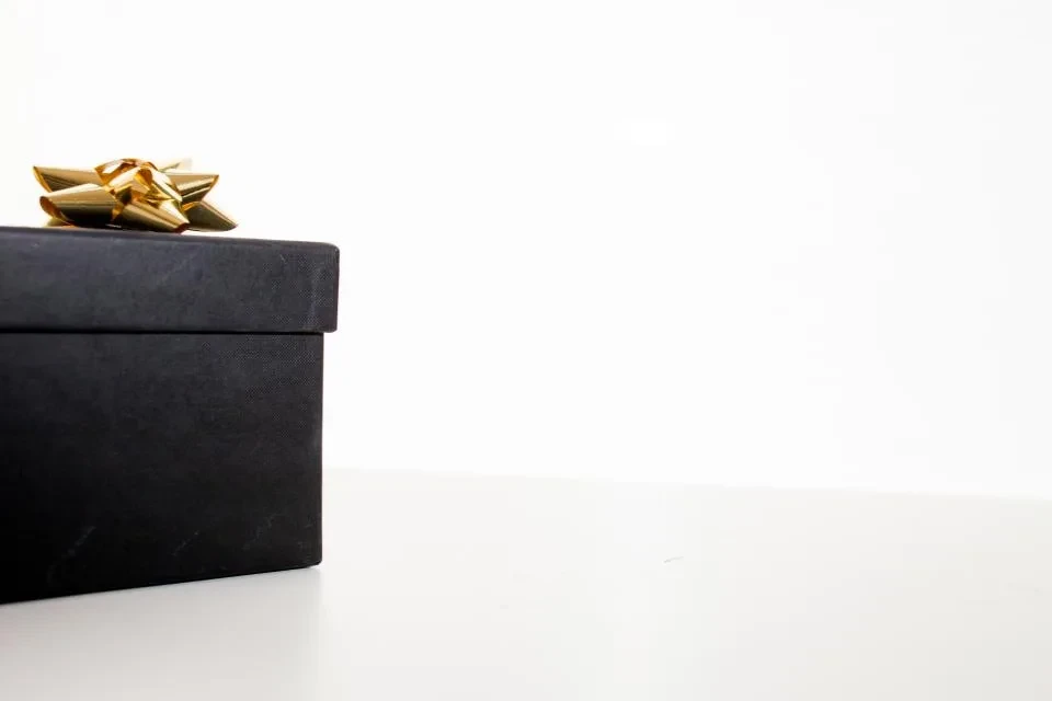 Una caja de regalo negra con un lazo dorado sobre una mesa blanca