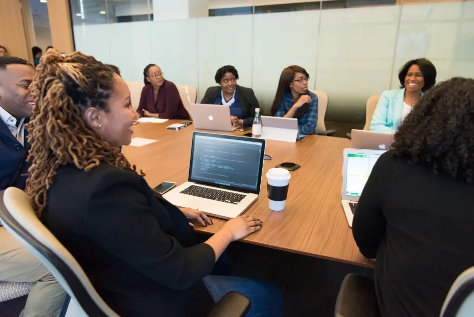 Un equipo diverso trabaja con portátiles alrededor de una mesa de reuniones